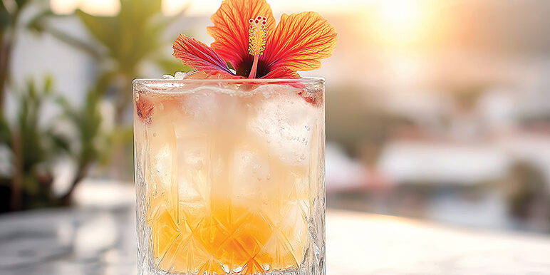 Glass with ice and orange cocktail decorated with hibiscus flower on marble table, with blurred cityscape and sunset in background mindful drinking