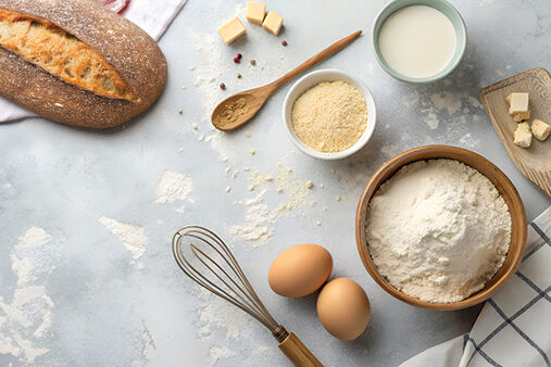 Fresh baking ingredients like flour, eggs, milk, and butter are neatly arranged on a dusty kitchen counter, ready for delicious homemade recipes. bakehouse